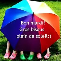 Un grand parapluie coloré abrite quatre paires de pieds chaussés de sandales vives sur l'herbe.