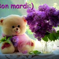 Un ours en peluche câlin tient un bouquet de fleurs violettes à côté d'une fenêtre ensoleillée.